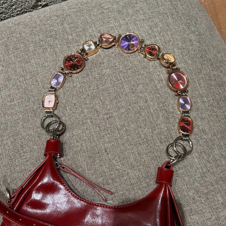 May include: A red leather handbag with a strap made of a chain of small, colorful watches.