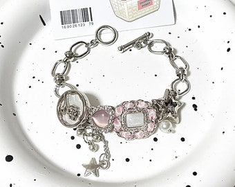 Könnte beinhalten: Ein silbernes Armband mit rosa und weißen Charms, darunter ein Stern, ein Herz und ein Quadrat mit Strasssteinen. Das Armband hat einen silbernen Verschluss und eine silberne Kette.