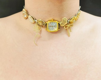 May include: A gold choker necklace with a variety of charms, including a small square watch, a flower, a bow, and several other decorative pieces.