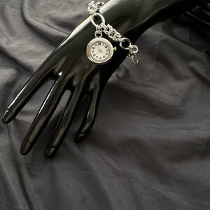 May include: A silver watch with a white face and black numbers on a silver chain bracelet.
