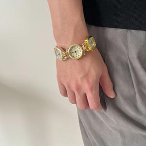 May include: A gold-toned bracelet with multiple square-shaped watches attached. The watches have white faces with black Roman numeral markings.