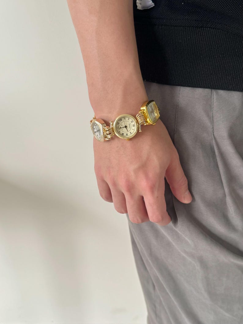 May include: A gold-toned bracelet with multiple square-shaped watches attached. The watches have white faces with black Roman numeral markings.