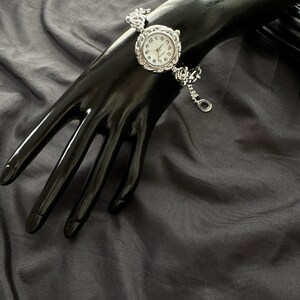 May include: A silver watch with a white face and black Roman numeral hour markers. The watch has a silver chain bracelet.