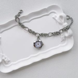 May include: A silver chain bracelet with a small round watch attached. The watch has a white face with black numbers and hands.