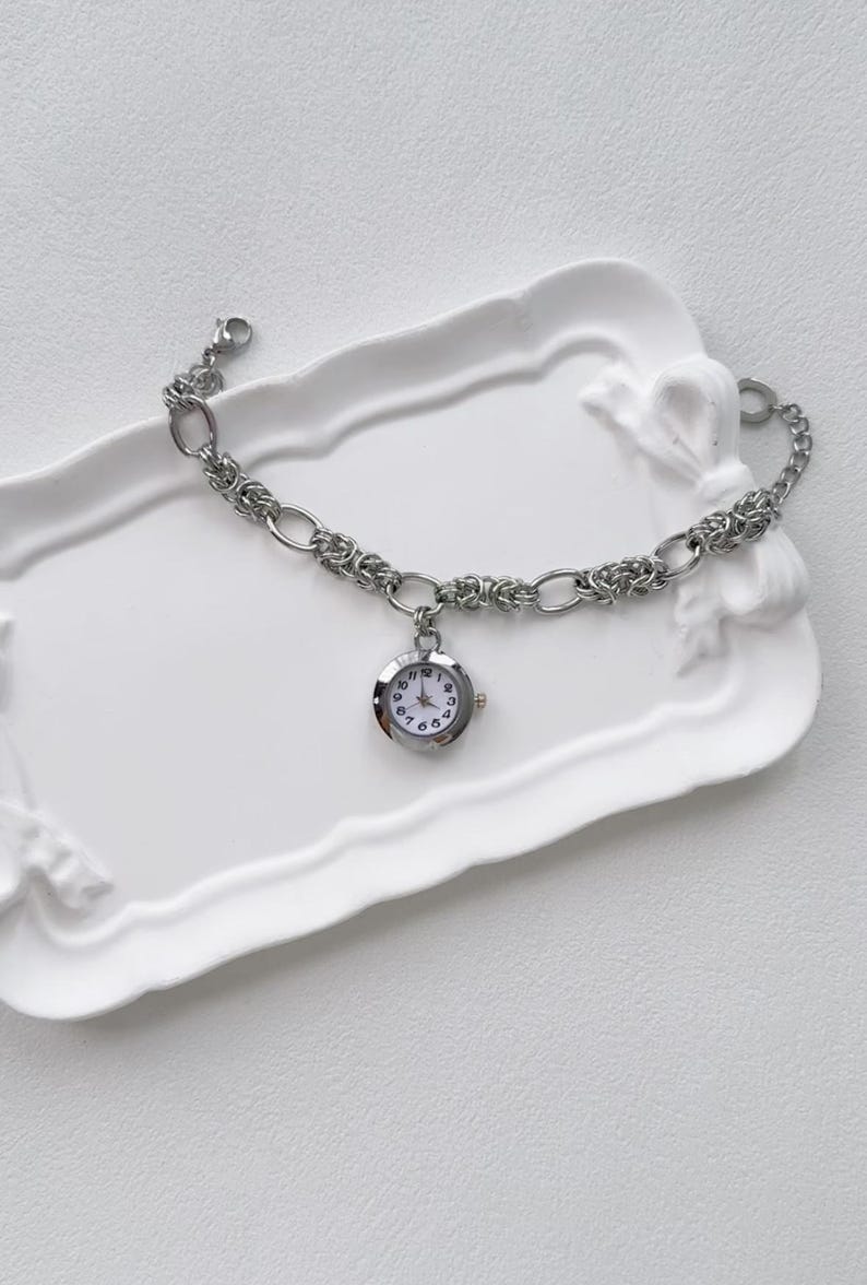 May include: A silver chain bracelet with a small round watch attached. The watch has a white face with black numbers and hands.