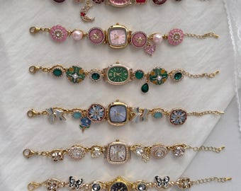 May include: A collection of six ornate, gold-toned bracelet watches. Each watch features a unique design with various colored watch faces, including pink, green, and gold. Embellishments include flowers, bows, and gemstones, creating a delicate and feminine aesthetic.