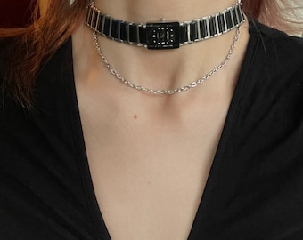 May include: A black choker necklace with a silver chain and a rectangular pendant with a black stone. The necklace is layered over a silver chain.