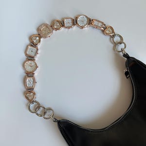 May include: A black leather handbag with a chain strap made of linked watch faces. The strap features a variety of watch faces, including round, square, and heart-shaped designs.