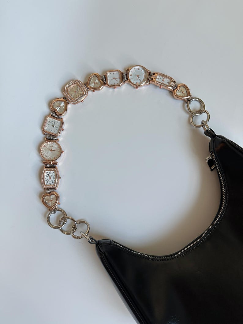 May include: A black leather handbag with a chain strap made of linked watch faces. The strap features a variety of watch faces, including round, square, and heart-shaped designs.
