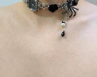 May include: A silver-toned choker necklace featuring a square watch face, black rose accents, and a large spider pendant. The spider has black gemstone accents and a dangling chain with a pearl and black teardrop bead.