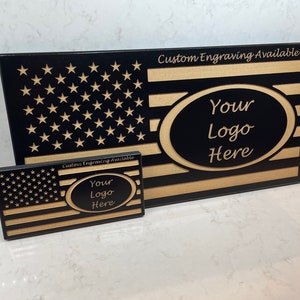 May include: Two black wooden plaques with a gold American flag design. The larger plaque has the text "Custom Engraving Available" and "Your Logo Here" in a gold oval. The smaller plaque has the text "Your Logo Here" in a gold oval.