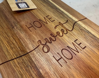 May include: A wooden cutting board with the words "Home Sweet Home" engraved on it. The board is made of acacia wood and has a natural finish.