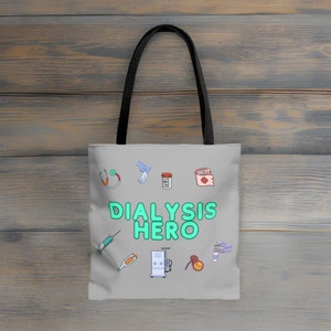 Puede incluir: Un bolso tote gris con asa negra, con ilustraciones médicas y las palabras "DIALYSIS HERO" en verde brillante. El bolso muestra imágenes de un estetoscopio, guantes, medicamentos, vendas, una jeringa, un termómetro y una máquina de diálisis.