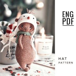 May include: Crochet pattern for a brown bear wearing a white snowman hat with a green scarf. The pattern is available in English and is a PDF download.
