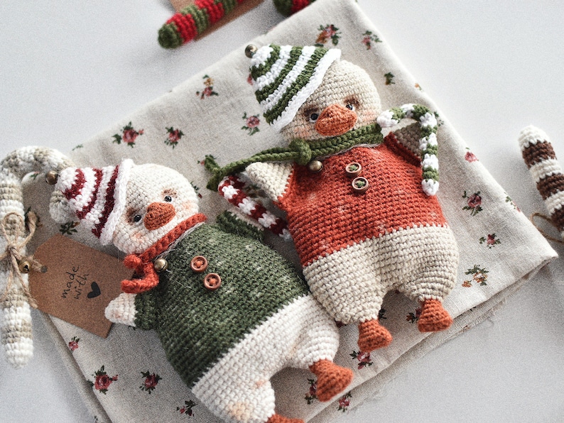 May include: Two crocheted penguin ornaments with red and white striped hats, one in green and white and the other in orange and white, with candy cane accents.  The text "made with love" is on a brown tag.