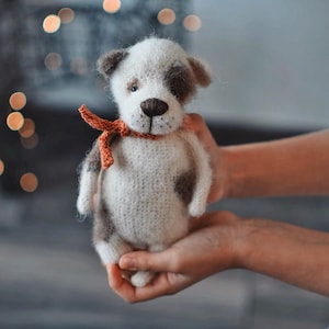 May include: A crocheted stuffed dog toy with brown and white fur, wearing a red ribbon around its neck.