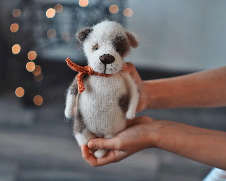 May include: A crocheted stuffed dog toy with brown and white fur, wearing a red ribbon around its neck.