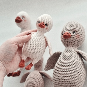 Pode incluir: Tr&ecirc;s brinquedos de peluche de pato feitos de croch&ecirc;. Um &eacute; branco com p&eacute;s e bico laranja, outro &eacute; castanho com p&eacute;s e bico laranja, e o terceiro &eacute; branco com p&eacute;s e bico laranja. Os patos s&atilde;o todos feitos &agrave; m&atilde;o e t&ecirc;m um aspeto bonito e caprichoso.