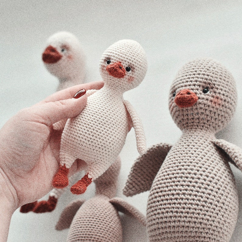 Pode incluir: Tr&ecirc;s brinquedos de peluche de pato feitos de croch&ecirc;. Um &eacute; branco com p&eacute;s e bico laranja, outro &eacute; castanho com p&eacute;s e bico laranja, e o terceiro &eacute; branco com p&eacute;s e bico laranja. Os patos s&atilde;o todos feitos &agrave; m&atilde;o e t&ecirc;m um aspeto bonito e caprichoso.