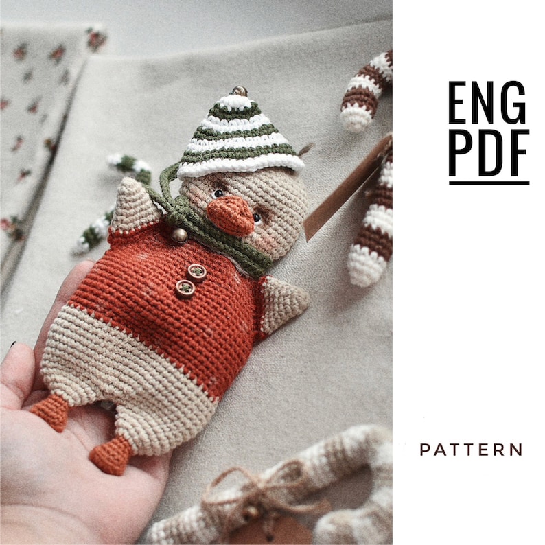 May include: Crochet pattern for a cute, brown and white duck wearing a green and white striped hat. The pattern is available in English and is a PDF download. The text "ENG PDF PATTERN" is visible in the image.