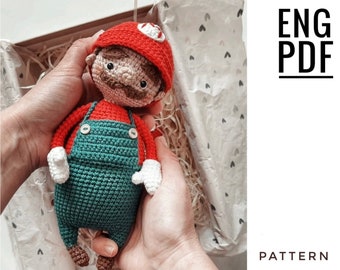 May include: Crochet pattern for a Super Mario character amigurumi doll. The doll is wearing a red hat, a green jumpsuit, and white gloves. The pattern is available in English and is a PDF download.