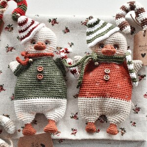 May include: Two crocheted snowman ornaments with candy cane accents. The snowman on the left is wearing a green and white outfit, while the snowman on the right is wearing a red and white outfit. Both snowmen have black eyes and a black button nose.