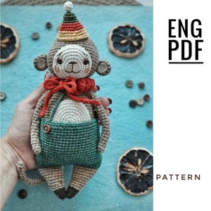 Op de afbeelding: Gehaakt aapje amigurumi speelgoed met een kleurrijke hoed en een overall. De aap heeft een rode strik en bruin garen haar.