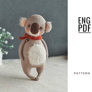 May include: A crocheted koala bear in brown, beige, and cream. The koala has a brown nose, small ears, and a red scarf. The image includes the text "ENG PDF" and "PATTERN".