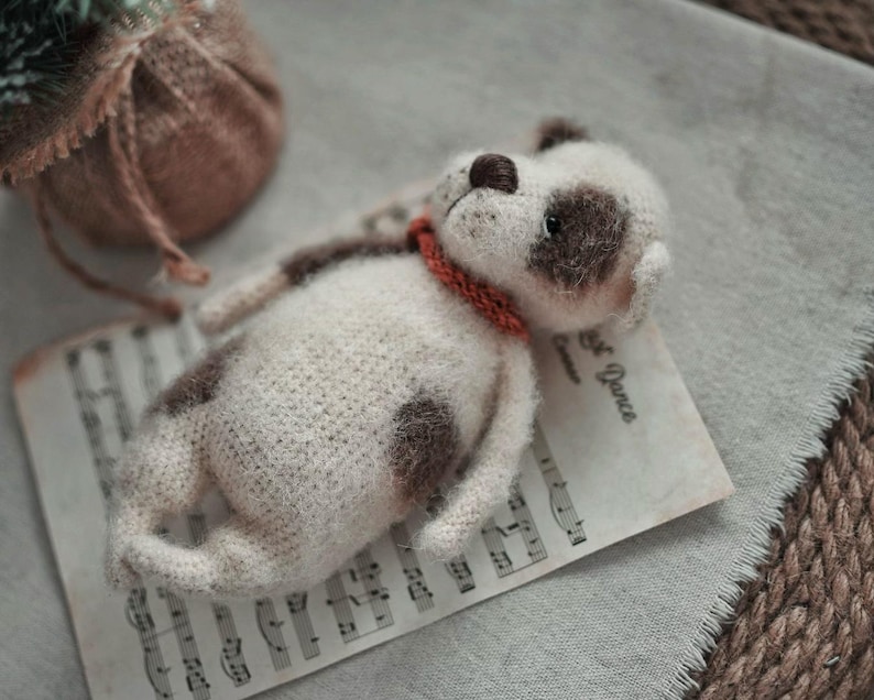 May include: A white and brown crocheted dog toy with a red collar lying on a sheet of music with the text "First Dance" printed on it.