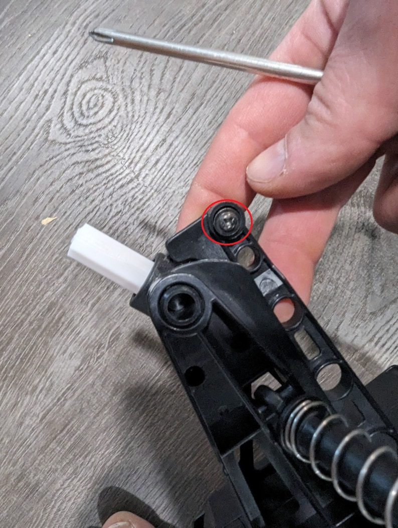 Puede incluir: Primer plano de una pieza de pl&aacute;stico negro con un muelle met&aacute;lico y un peque&ntilde;o tornillo plateado. El tornillo est&aacute; rodeado de un c&iacute;rculo rojo.