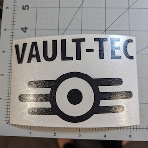 May include: Black and white sticker with the text "VAULT-TEC" and a stylized logo of a circle with three lines radiating from it.