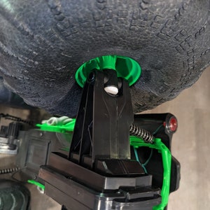 Puede incluir: Primer plano de un cami&oacute;n de juguete negro y verde con grandes ruedas negras. El cami&oacute;n tiene un sistema de suspensi&oacute;n negro y un bot&oacute;n rojo en el lateral.
