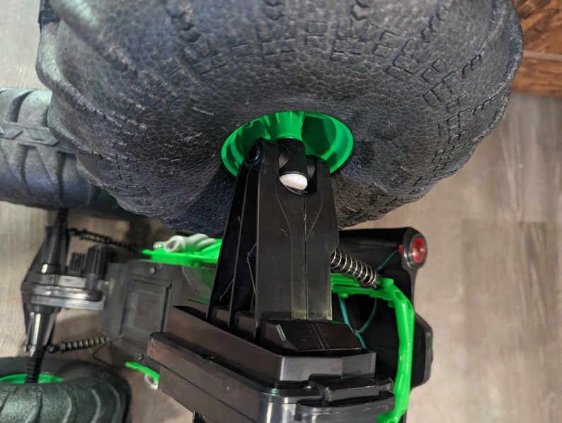 Puede incluir: Primer plano de un cami&oacute;n de juguete negro y verde con grandes ruedas negras. El cami&oacute;n tiene un sistema de suspensi&oacute;n negro y un bot&oacute;n rojo en el lateral.