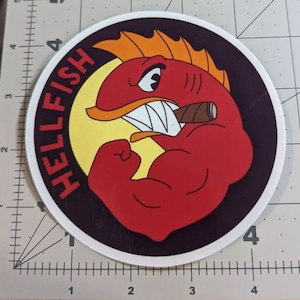 Peut inclure: Un autocollant rond avec un fond noir et un poisson rouge de dessin animé avec un cigare dans la bouche. Le poisson a un ventre jaune et fléchit son biceps. Le texte "HELLFISH" est écrit en blanc autour du poisson.