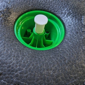 May include: Close-up of a black tyre with a green rim and a white plastic centre cap.
