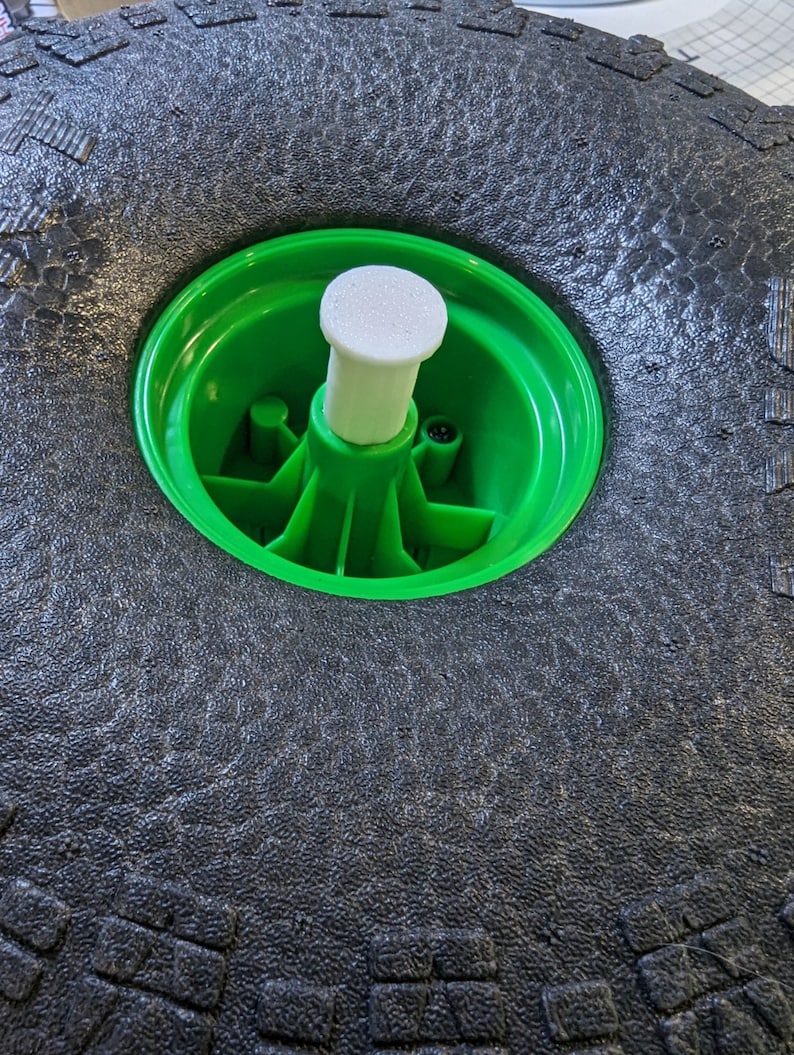 Puede incluir: Primer plano de un neum&aacute;tico negro con una llanta verde y un tap&oacute;n central de pl&aacute;stico blanco.