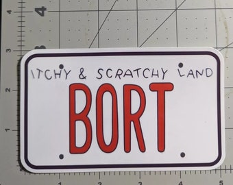 Puede incluir: Una placa de matrícula blanca con texto negro y borde negro. El texto en la placa dice "ITCHY & SCRATCHY LAND" y "BORT" en letras rojas.