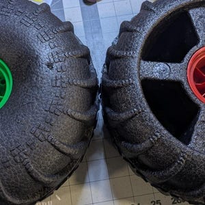 Puede incluir: Dos ruedas inflables de espuma negra para un carro de playa. La rueda de la izquierda tiene un cubo central verde y el texto "Old Model" escrito debajo. La rueda de la derecha tiene un cubo central rojo.