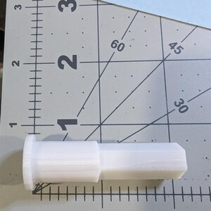 Puede incluir: Un conector de pl&aacute;stico blanco con forma cil&iacute;ndrica y un extremo ligeramente inclinado. El conector mide aproximadamente 5 cm de largo.