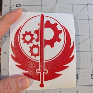 May include: Red vinyl decal of the Fallout video game logo. The logo features a stylized winged symbol with a sword and three gears.