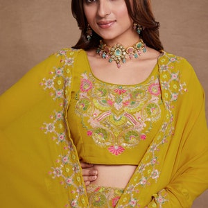 May include: A mustard yellow embroidered top with a floral design. The top has a scoop neckline and short sleeves. The model is wearing a matching skirt and jewelry.