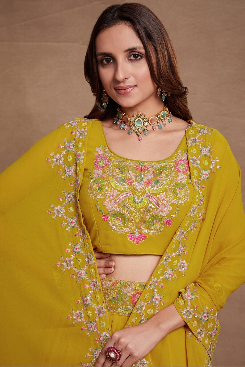 May include: A mustard yellow embroidered top with a floral design. The top has a scoop neckline and short sleeves. The model is wearing a matching skirt and jewelry.