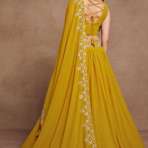 May include: A mustard yellow maxi skirt with a floral embroidered waistband and a matching yellow dupatta with a white and pink floral embroidered border. The dupatta has tassels on the edges.