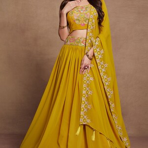 May include: A mustard yellow lehenga with floral embroidery and a matching crop top. The outfit includes a sheer dupatta with floral embroidery and tassels.
