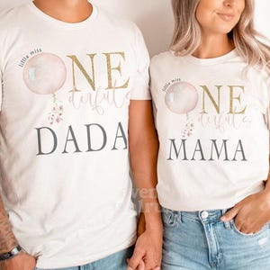 May include: Two white t-shirts with the text "Little Miss One Derful" and a pink balloon graphic. The text "Dada" is on one shirt and "Mama" is on the other.