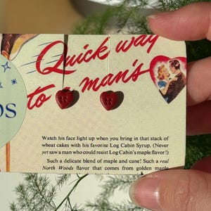 May include: A vintage-style card with the text "Cozy Keeps" and "Quick way to man's". The card features heart-shaped buttons and a couple in a heart. The card also has text about maple syrup.