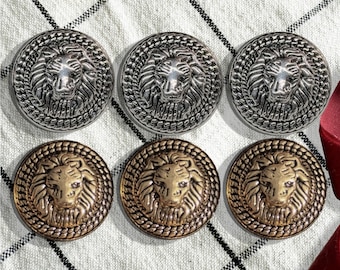 May include: Six round metal buttons with a lion head design. Three buttons are silver and three buttons are gold.