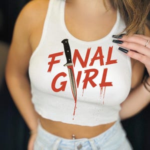 Könnte beinhalten: Weißes geripptes Crop-Top mit den roten Worten "FINAL GIRL" und einer Messer-Grafik. Das Messer scheint mit rotem Blut zu tropfen. Das Top ist ärmellos.