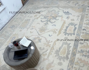 May include: A cream-colored rug with a traditional Persian design in shades of gray, beige, and pink. The rug is on a wooden floor and there are two brown poufs in the foreground. The text "FUSIONRUGSTORE" appears three times in the image.
