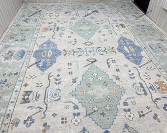 Könnte beinhalten: Ein hellgrauer Teppich mit einem blauen, grünen und braunen geometrischen Muster. Der Teppich hat einen Used-Look und einen dezenten Glanz.